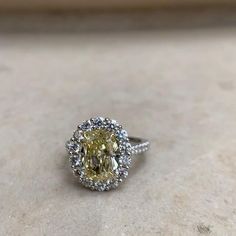 a fancy yellow diamond ring sitting on top of a stone surface with diamonds around it