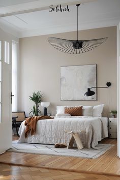 a bedroom with a white bed, wooden floors and an art piece on the wall