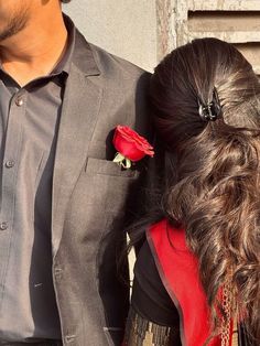 a man standing next to a woman with a rose in her lap and wearing a suit