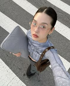 a woman in glasses is holding a pillow on the crosswalk while looking at the camera