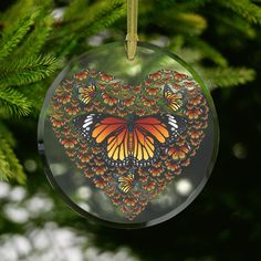 a glass ornament shaped like a heart with butterflies on it hanging from a tree