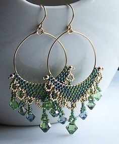 a pair of green and blue beaded hoop earrings on a white vase next to a cup