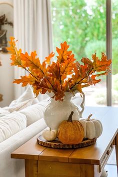 a white vase filled with orange leaves on top of a table next to a window