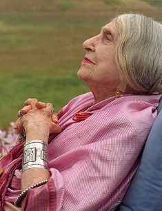 an older woman sitting in a chair looking off into the distance with her hands clasped