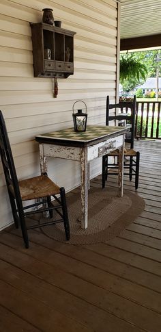 an old table and two chairs are on the porch next to a wall mounted clock