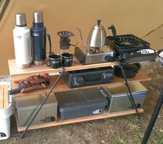 an outdoor camping table with coffee pots, kettles and other items sitting on it