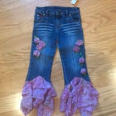 a pair of blue jeans with pink flowers on the side and ruffles at the bottom