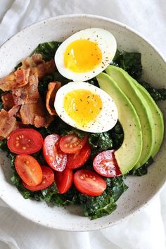 a white bowl filled with bacon, avocado, tomatoes and hard boiled eggs