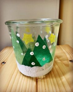 a glass bowl with paper trees and stars painted on the inside is sitting on a wooden table