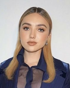 a woman with long blonde hair wearing a blue suit and matching earrings is looking at the camera