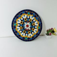 a colorful plate sitting on top of a table next to a vase with flowers in it