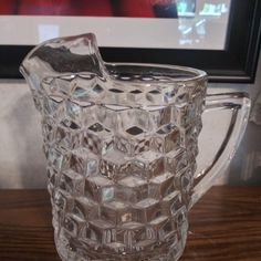 a clear glass pitcher sitting on top of a wooden table next to a framed photo