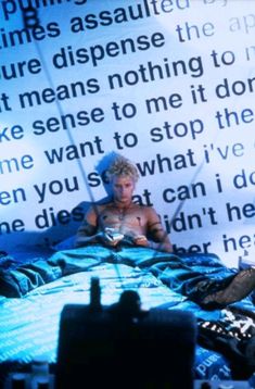 a man sitting on top of a bed in front of a wall with words behind him