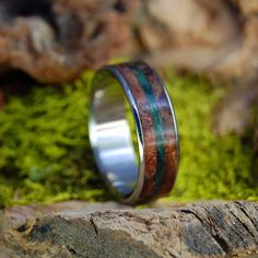 a wedding ring with wood and green inlays on top of mossy rocks