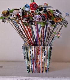 a vase filled with lots of different colored pencils and paper flowers on top of a table