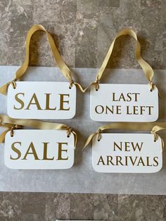 four sale tags with gold ribbons on them sitting on a marble floor next to a wall