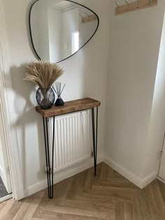 a wooden table sitting next to a mirror on top of a white wall in a room