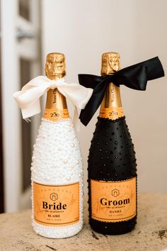 two champagne bottles with black and gold ribbons tied to them, sitting on a table