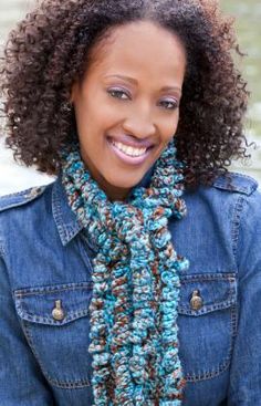 a woman wearing a blue jean jacket and a crocheted scarf smiles at the camera