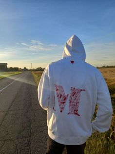 a person wearing a white hoodie with the letter m on it is walking down an empty road