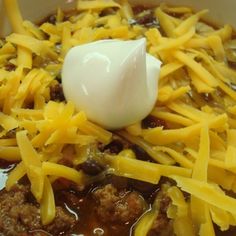 a bowl full of chili and cheese with an egg on top in the middle, ready to be eaten