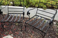 two metal chairs sitting next to each other on top of mulch covered ground in front of a planter