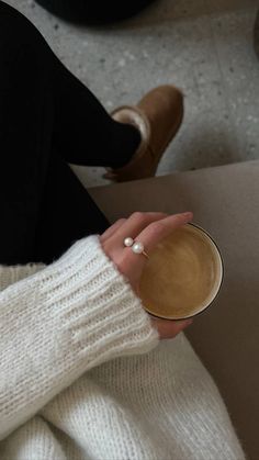 a woman in white sweater holding a cup of coffee with her right hand on top of the cup