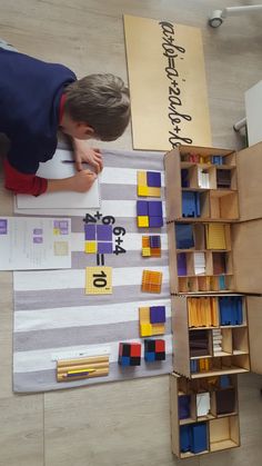 a young boy is writing on a piece of paper in front of some bookshelves