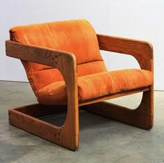 an orange chair sitting on top of a cement floor next to a white wall with a wooden frame