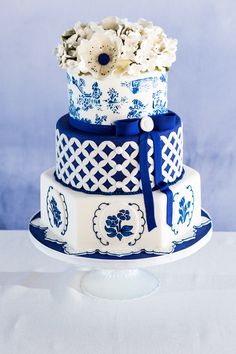 a three tiered cake with blue and white designs on it's sides, decorated with flowers