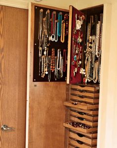 a closet filled with lots of necklaces and bracelets hanging on the wall next to a door