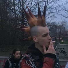 a man with spiked hair and chains on his head is talking on a cell phone