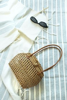 a straw bag sitting on top of a bed next to sunglasses