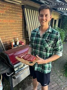 a man standing in front of a bbq holding a tray of meat on it