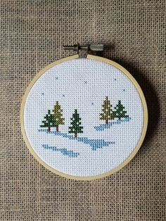 a cross - stitch christmas scene with trees in the snow on a beige fabric background