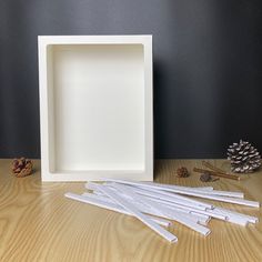 a white square frame sitting on top of a wooden table next to some pine cones