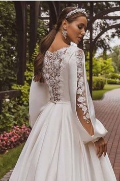 a woman wearing a wedding dress with long sleeves and an open back, standing on a brick