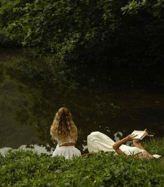 two women are sitting by the water reading