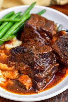 a white plate topped with meat and potatoes covered in gravy next to green beans