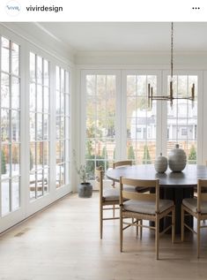 a dining room table with chairs and vases on top of it in front of large windows