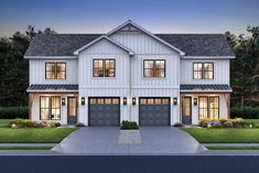 a white house with two garages and windows in the front yard at night time