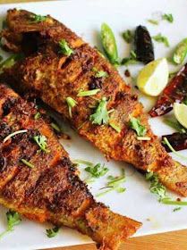 two grilled fish on a white plate with lemon wedges and cilantro