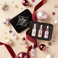 christmas ornaments and cosmetics are arranged on a pink background with red ribbon, ornament, and star decorations