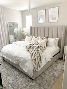 a large bed with white sheets and pillows in a bedroom next to a mirror on the wall