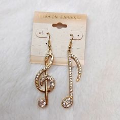 a pair of earrings with musical notes and crystals in gold plated metal, sitting on a white furnishing