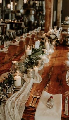 a long wooden table with candles and flowers on it, along with napkins and place settings