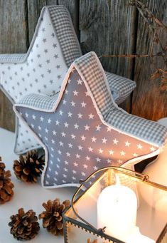 a white and gray star shaped candle holder next to some pine cones on a table