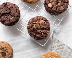 four chocolate chip cookies cooling on a wire rack next to newspaper paper and a cup of coffee