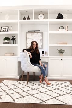 a woman sitting on a chair in front of a white bookcase with shelves behind her