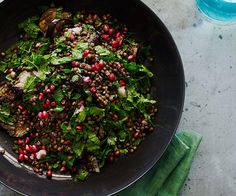 a bowl filled with greens and pomegranates on top of a table